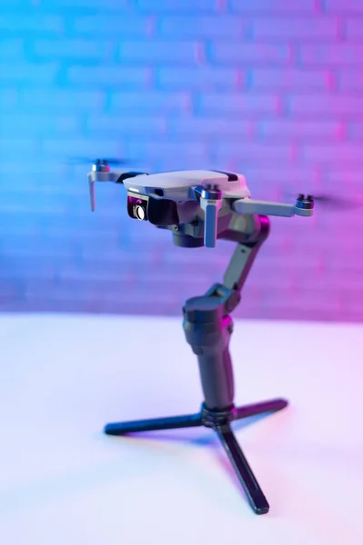 Un quadrocopter con una cámara Drone. Un pequeño quadcopter no tripulado se encuentra en un soporte estabilizador para un teléfono contra una hermosa pared de ladrillo de neón — Foto de Stock
