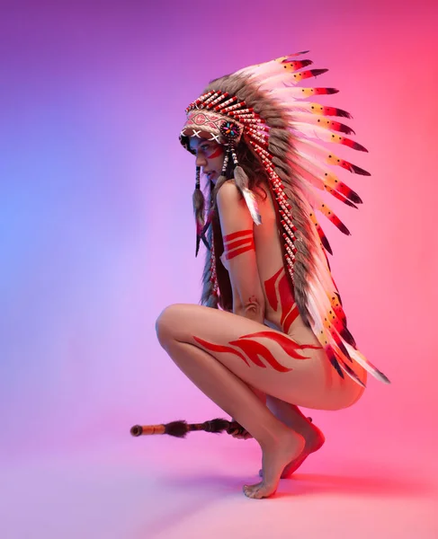 Naked woman in native american costume with feathers on a neon background — Stock Photo, Image