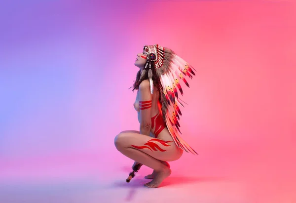 Naked woman in native american costume with feathers on a neon background — Stock Photo, Image
