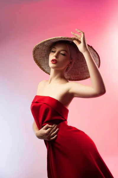 Uma menina bonita nova em um tecido vermelho e um chapéu triangular asiático em um fundo rosa — Fotografia de Stock