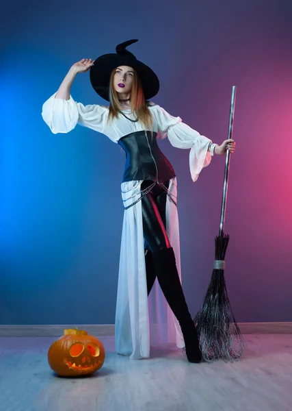 Cadılar Bayramı için elinde süpürge ve balkabağıyla cadı kostümü giymiş ince bir kız. — Stok fotoğraf