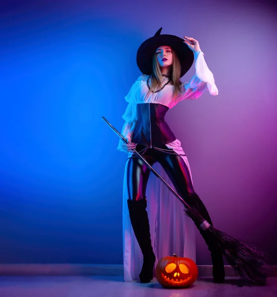 Chica delgada en un disfraz de bruja para Halloween con una escoba y una calabaza — Foto de Stock