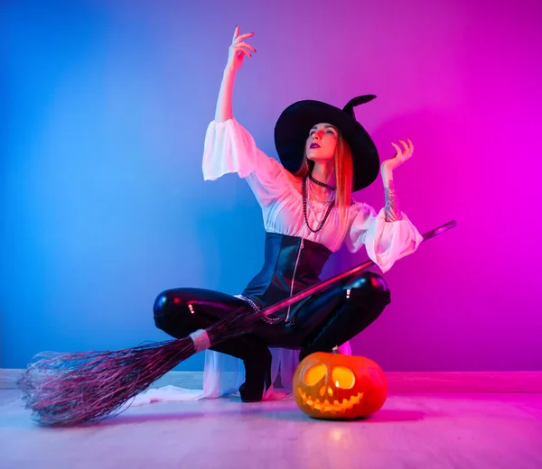 Chica delgada en un disfraz de bruja para Halloween con una escoba y una calabaza —  Fotos de Stock
