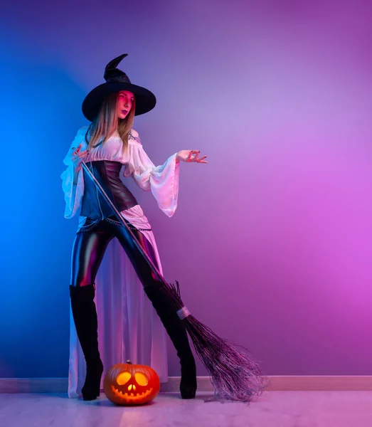 ハロウィンの魔女の衣装を着た女の子ネオンライトのほうきとカボチャで — ストック写真