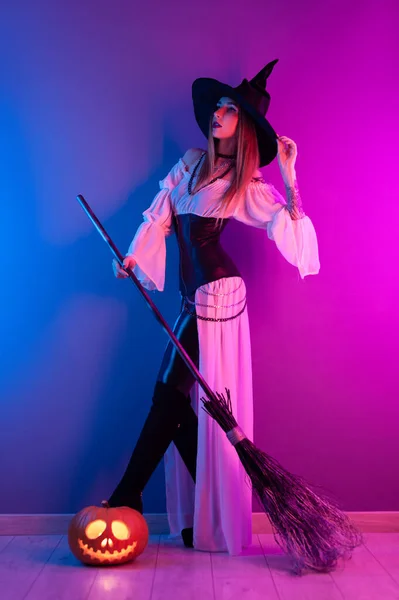 Une fille en costume de sorcière pour Halloween avec un balai et une citrouille au néon — Photo