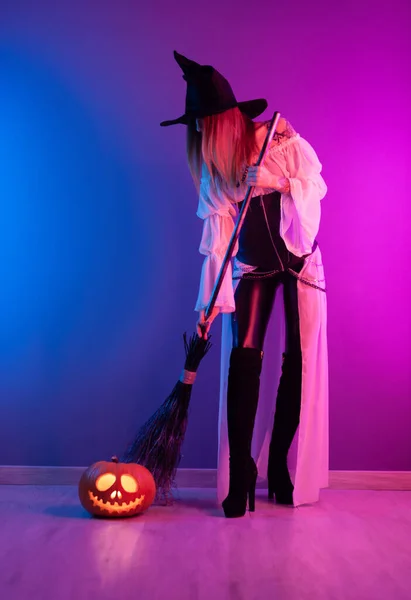 Une fille en costume de sorcière pour Halloween avec un balai et une citrouille au néon — Photo