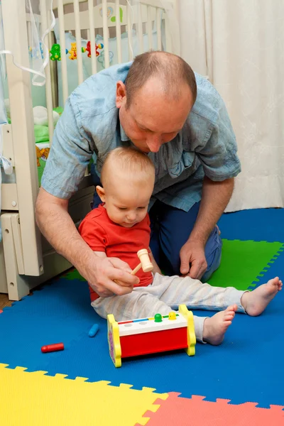 El niño juega con el padre un juguete de madera con un martillo y el — Foto de Stock