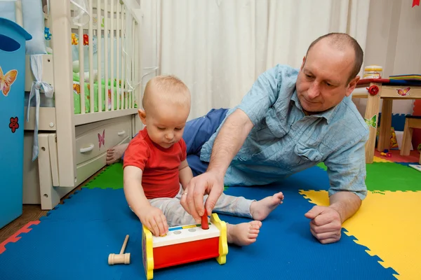 El niño juega con el padre un juguete de madera con un martillo y el — Foto de Stock