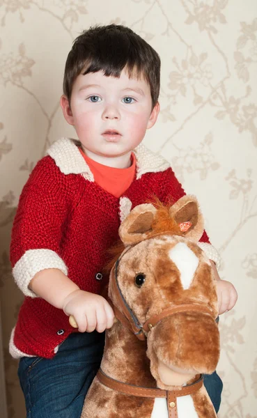 El muchacho se sienta sobre el juguete del caballo en la habitación —  Fotos de Stock