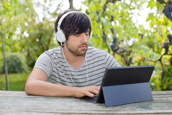Młody mężczyzna pracujący z tabliczka pc słuchania muzyki w słuchawkach — Zdjęcie stockowe
