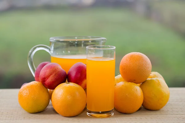 Glasses of orange juice and peaches on wooden table outdoor — Stock Photo, Image