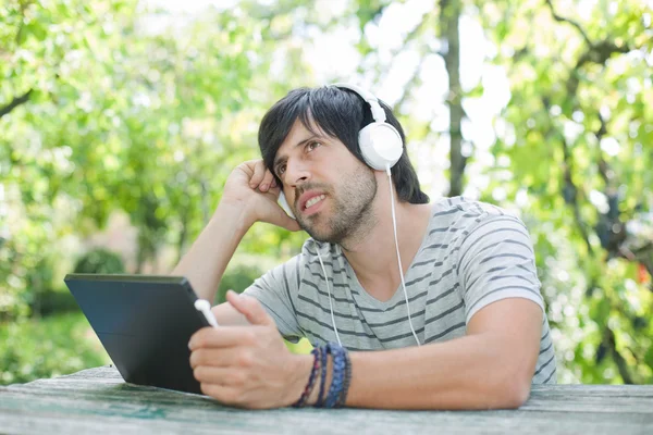 Junger Mann arbeitet mit einem Tablet-PC und hört Musik mit Kopfhörern — Stockfoto