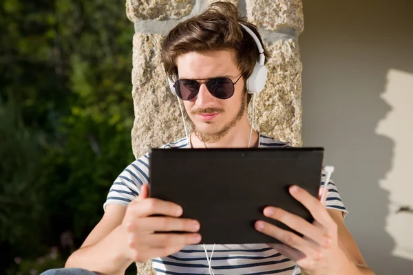 Giovane uomo che si rilassa con un tablet pc ascoltando musica con cuffie — Foto Stock