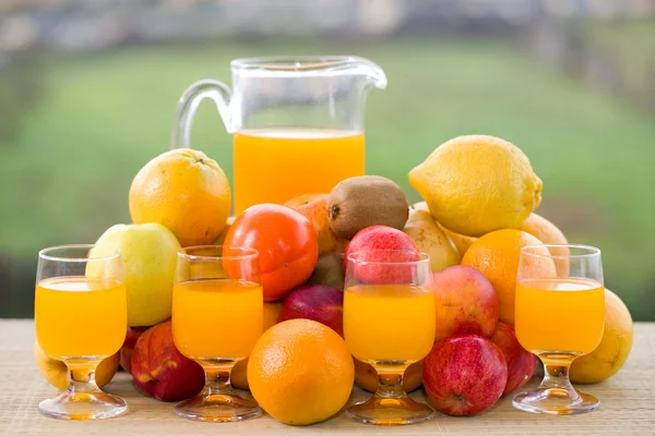 Glazen sinaasappelsap en een heleboel fruit op houten tafel buiten — Stockfoto