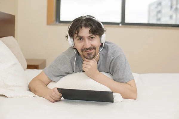 Homem usando um computador tablet enquanto deitado no quarto — Fotografia de Stock