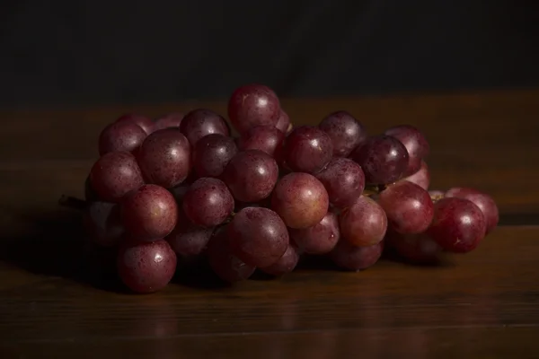 Eine Traube roter Trauben vor hölzernem Hintergrund — Stockfoto