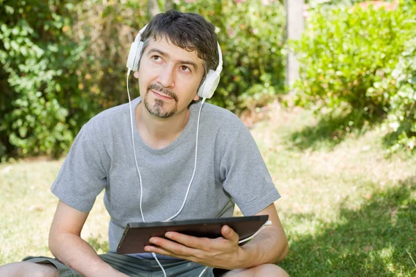 Jonge man met een tablet met koptelefoon, buiten — Stockfoto