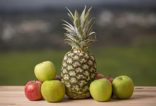 Ananas och äpple på bord av trä, utomhus — Stockfoto