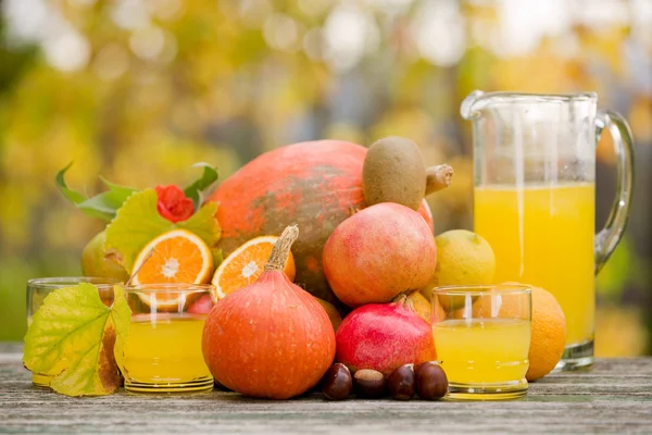 Copos de suco e muitas frutas de outono na mesa de madeira, ao ar livre — Fotografia de Stock