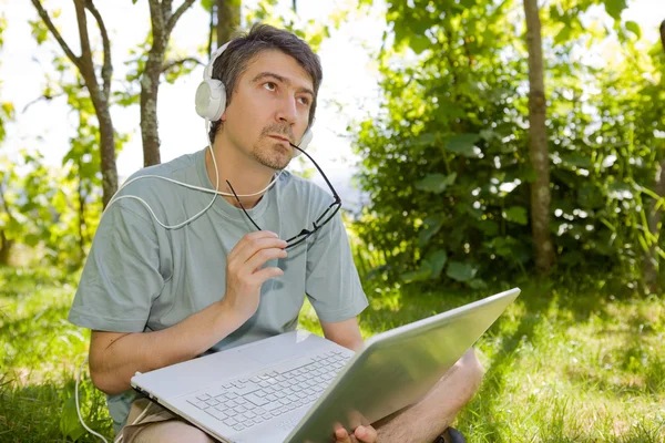 Uomo seduto sull'erba che lavora con un computer portatile — Foto Stock