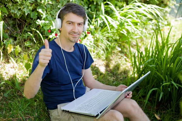 Bir dizüstü bilgisayar ile çalışma çimenlerin üzerinde oturan adam — Stok fotoğraf
