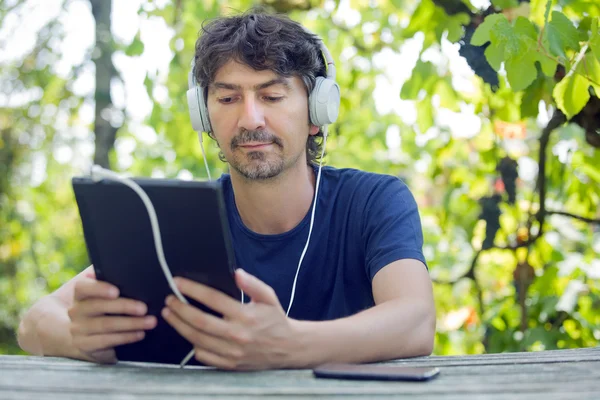 Young man holding a tablet with headphones, outdoor — Stock Photo, Image