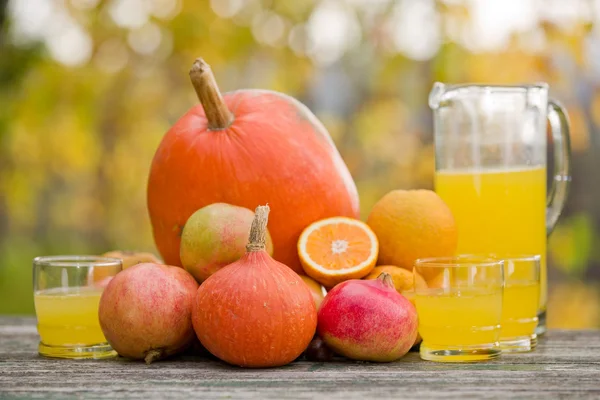 Saftgläser und jede Menge Herbstfrüchte auf Holztisch, draußen — Stockfoto