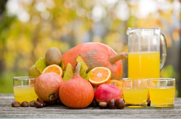 Saftgläser und jede Menge Herbstfrüchte auf Holztisch, draußen — Stockfoto