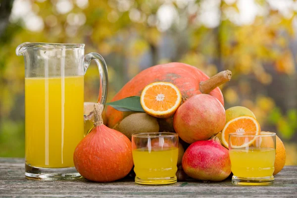 Saftgläser und jede Menge Herbstfrüchte auf Holztisch, draußen — Stockfoto