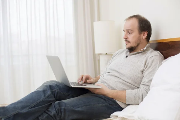 Uomo a letto che lavora con un computer portatile — Foto Stock