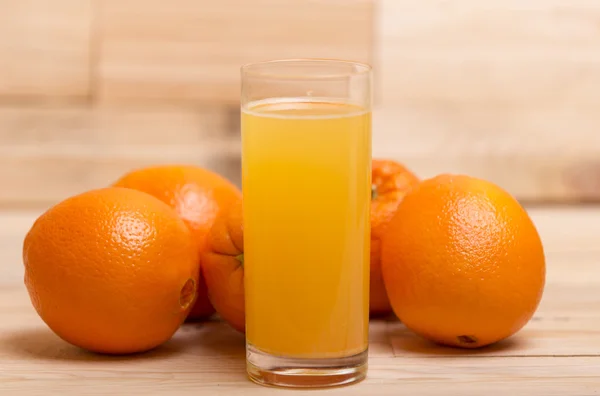 Copo de suco de laranja fresco e laranjas em um fundo de madeira — Fotografia de Stock