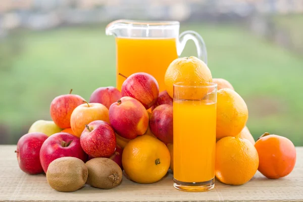 Vasos de jugo de naranja y muchas frutas en la mesa de madera al aire libre —  Fotos de Stock