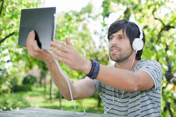 Young man putting out hand with digital tablet while sitting on a table — Stock Photo, Image