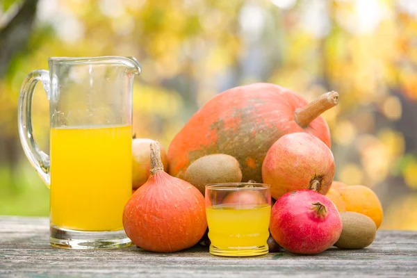 Copos de suco e muitas frutas de outono na mesa de madeira, ao ar livre — Fotografia de Stock