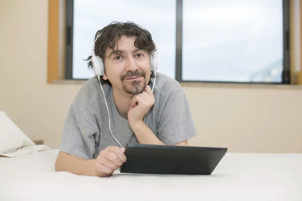 Homem usando um computador tablet enquanto deitado no quarto — Fotografia de Stock