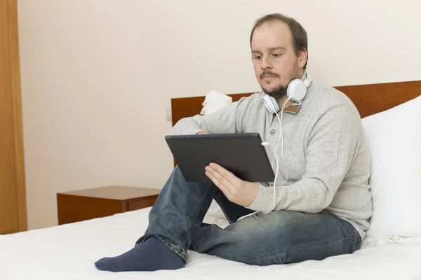 Casual man working with a tablet pc in bed — Stock Photo, Image