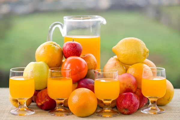 Glazen sinaasappelsap en een heleboel fruit op houten tafel buiten — Stockfoto