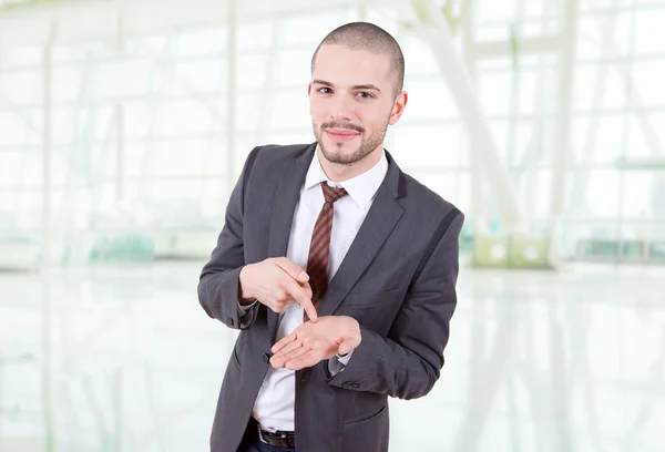 Jovem empresário apontando para sua mão, no escritório — Fotografia de Stock