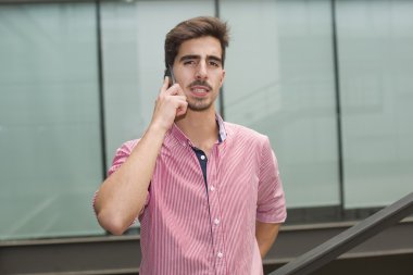 Bir ofis binasının içinde telefonla konuşan sıradan bir genç.