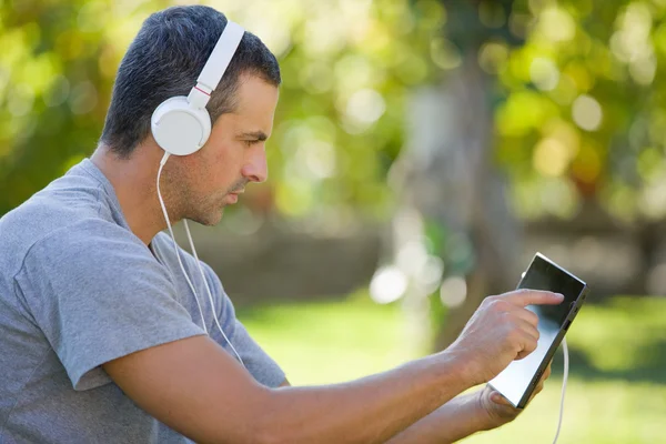 Giovane uomo che si rilassa con un tablet pc ascoltando musica con cuffie su un parco — Foto Stock