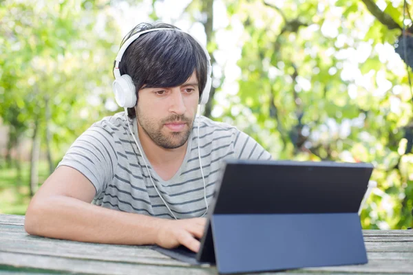 Giovane che lavora con un tablet pc ascoltando musica con le cuffie — Foto Stock