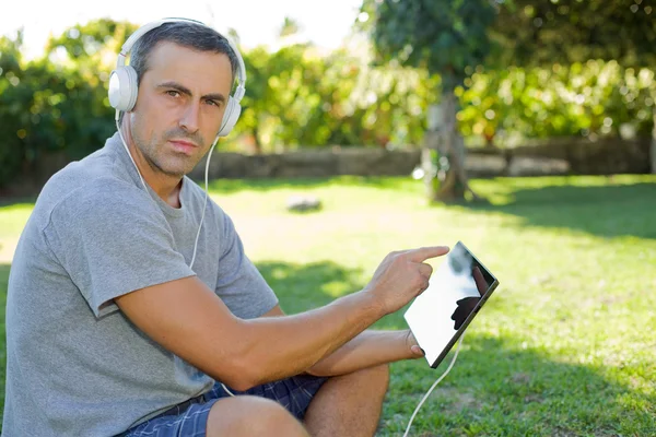 Giovane che si rilassa con un tablet pc ascoltando musica con le cuffie — Foto Stock