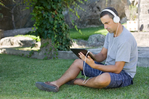 Giovane che si rilassa con un tablet pc ascoltando musica con le cuffie — Foto Stock