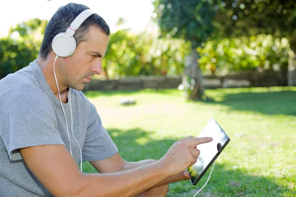 Giovane che si rilassa con un tablet pc ascoltando musica con le cuffie — Foto Stock