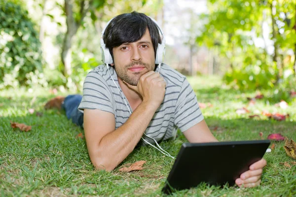 Giovane che si rilassa con un tablet pc ascoltando musica con le cuffie — Foto Stock