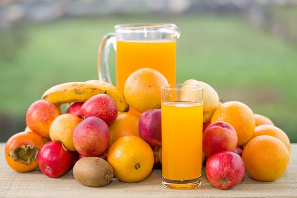 Orangensaft und viel Obst auf Holztisch im Freien — Stockfoto