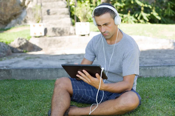 Giovane che si rilassa con un tablet pc ascoltando musica con le cuffie — Foto Stock