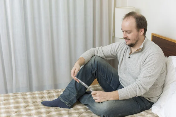 Homem casual trabalhando com um tablet pc na cama — Fotografia de Stock