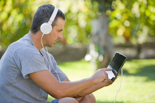 Giovane che si rilassa con un tablet pc ascoltando musica con le cuffie — Foto Stock