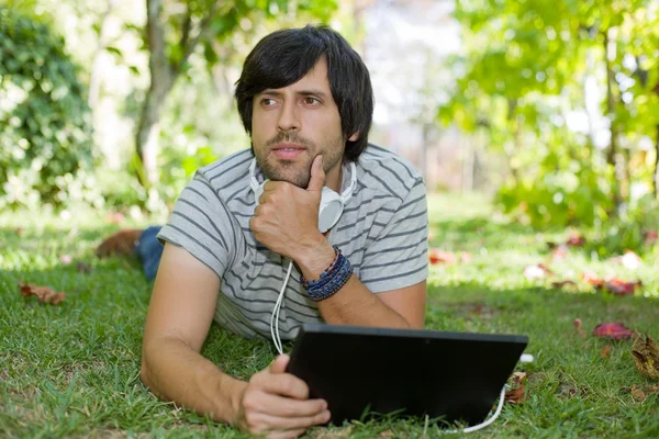Молодий чоловік розслабляється з планшетним ПК, слухаючи музику з навушниками — стокове фото